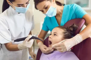 Julho Laranja Campanha Duas profissionais de saúde atendendo uma criança em uma clínica odontológica, realizando tratamento dental com equipamentos modernos.