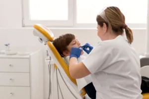 ampanha Julho Laranja Dentista Ortodontista realizando manutenção na boca de uma criança no consultório odontológico, com cuidado e atenção ao procedimento.